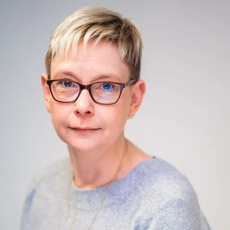 Mitarbeiterporträt einer Frau mit Brille vor hellem Hintergrund